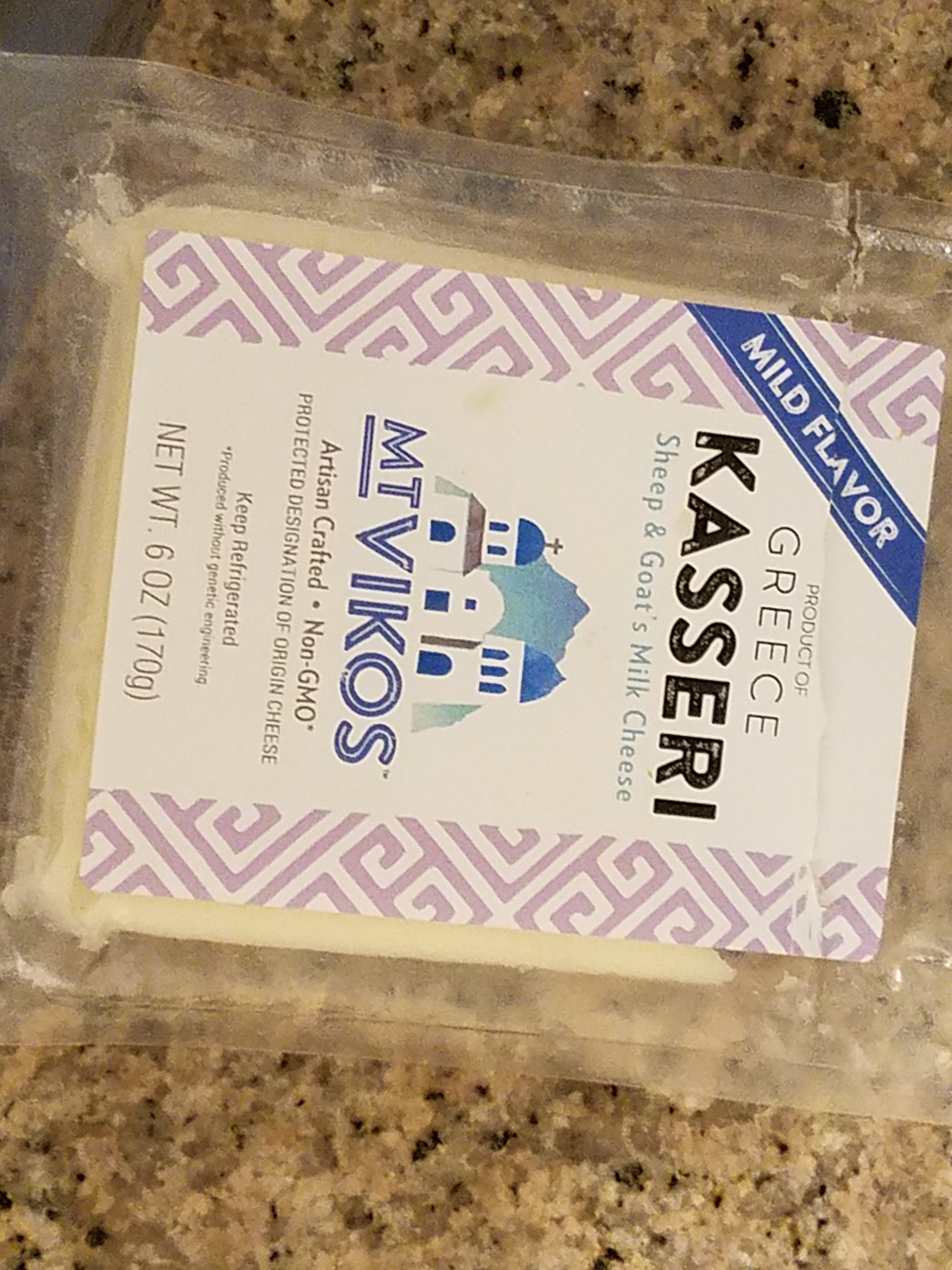 Living well in the 21st century. Limassol, Cyprus. A plastic container containing kasseri cheese. Product of Greece. Mt Vikos - artisan crafted, non-gmo, net wt. 6 oz (170g). 