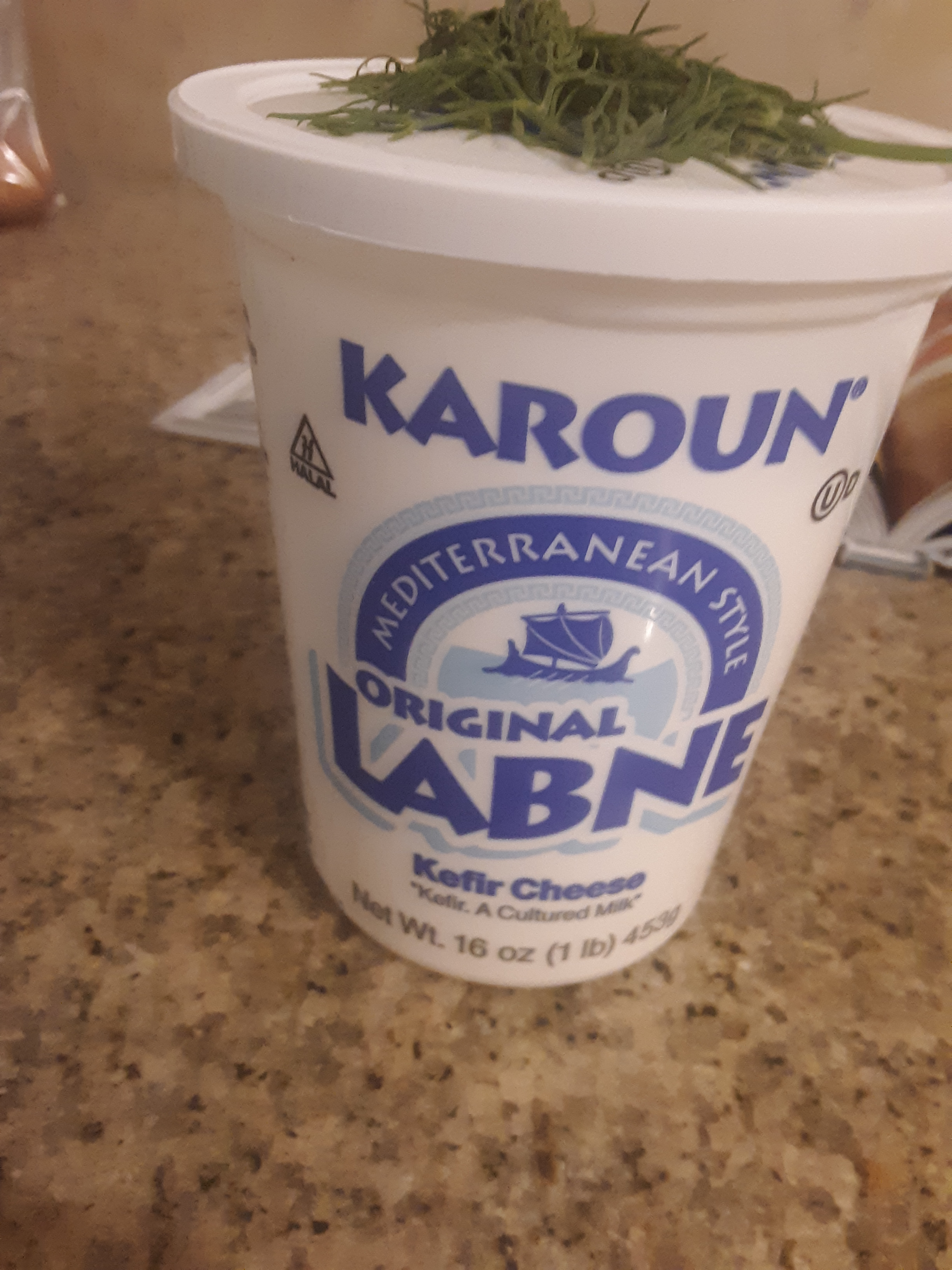 Living well in the 21st century - Limassol, Cyprus - picture of a white container with a blue label written on the container, "karoun -mediterranean style - original Lebne - kefir cheese - "kefir. A cultured milk." Net wt. 16 oz (1 ib) 453g placed on a brown kitchen counter. 