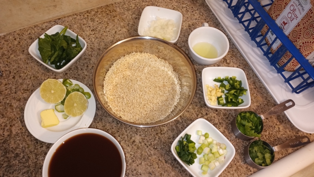 Living well in the 21st century. Limassol, Cyprus. Rice in a big mixing bowl, 2 - 3 garlic, 1 green chiles, 1 bunch cilantro, 1 bunch parsley, 1 lime, 1 tbsp unsalted butter, 2 - 3 tbsp grapeseed oil (or any other neutral oil), 1 yellow onions, 1 cup spinach, and 2 cups vegetable stock. All are in small containers. 