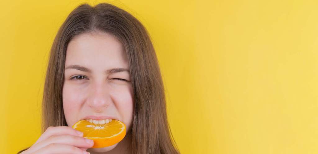 Living well in the 21st century-Limassol, Cyprus. An orange background with a girl biting into an orange, and making a face. 